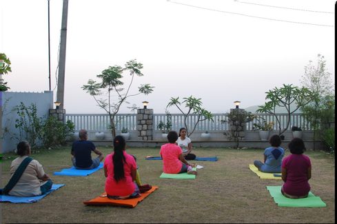 Practitioners seated on mats on a terrace facing the mountains